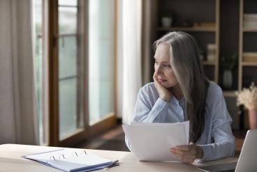 Older person sitting at desk reviewing paperwork and looking thoughtful