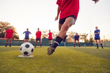 A female football player kicks a ball with her team looking on